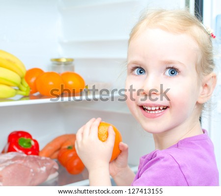 Happy smiling little girl holding orange on open fridge background
