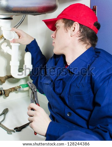Plumber in uniform repairing pipeline in the house.