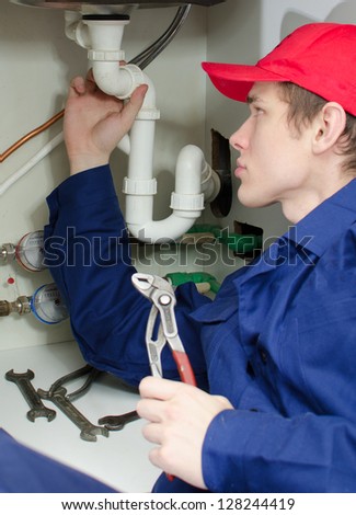 Plumber in uniform repairing pipeline in the house.
