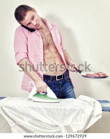 Young man with pan and phone ironing his shirt