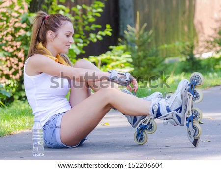 Young female skater sitting on the road and ties her rollers