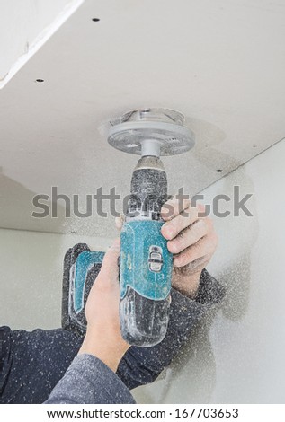 Male hands cuts hole under light bulb