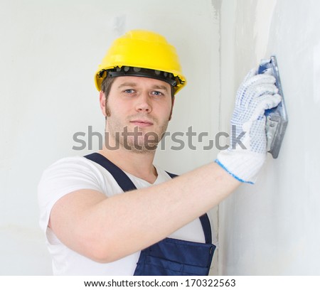 Male plasterer in hard hat polishing the wall.