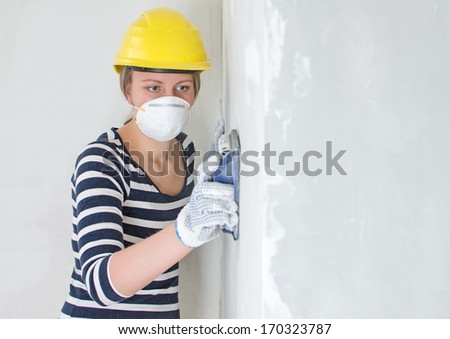 Female plasterer in hard hat polishing the wall. Place for your text.
