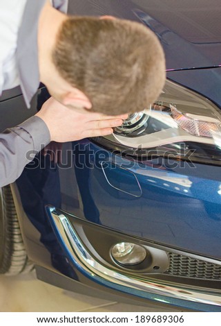 Mechanic wipes car headlight at car service.
