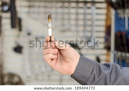 Spark plug in hand against the cabinet with tools.