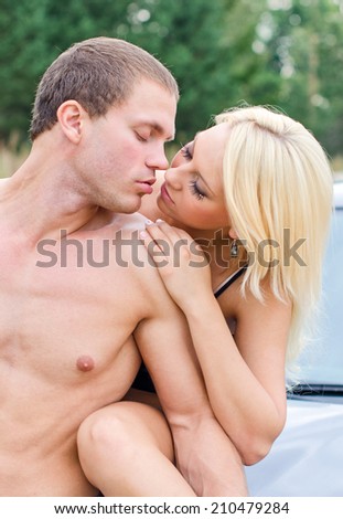 Sexy young couple kissing on the car\'s hood.
