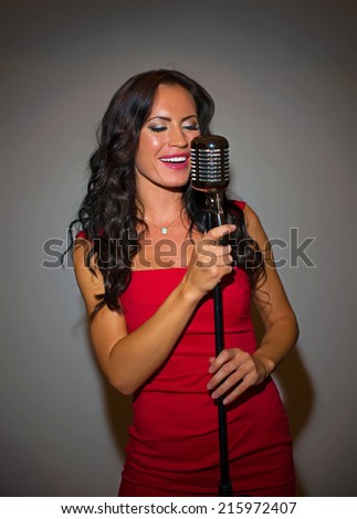 Attractive brunette woman singing into vintage microphone.