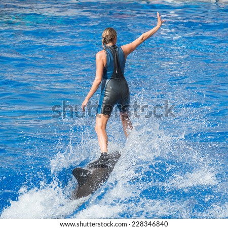 Woman-trainer riding on dolphin in water pool.