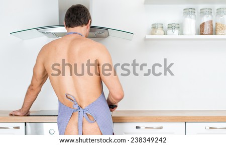 Naked man preparing food in the kitchen. View from the back.