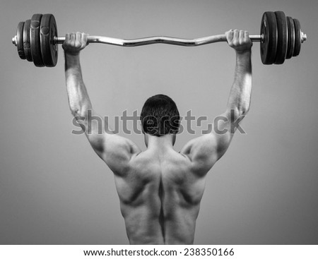 Muscular man doing exercises with barbell. Back view. Black and white.