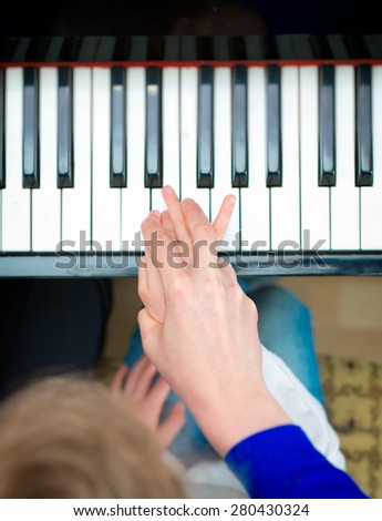 Woman teaching little girl to play the piano. Top view.