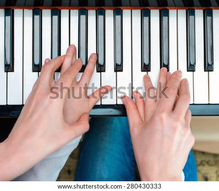 Woman teaching little girl to play the piano. Top view.