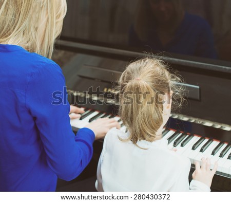 Woman teaching little girl to play the piano. Back view.
