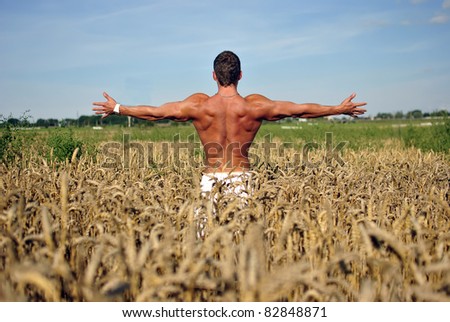 bodybuilder with arms wide open with sunglasses standing waist-deep in the field