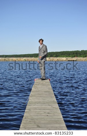 man in a gray business suit standing on a pier near the sea