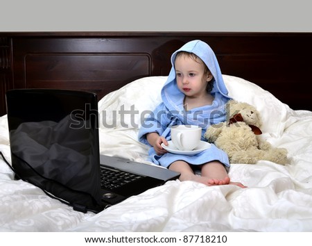 little girl in a bathrobe relaxing on the bed after a shower with cup of tea and laptop