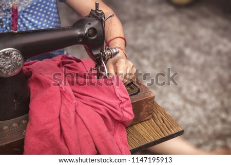 Indian Senior  women sitting cross-legged making clothes with old sewing machine