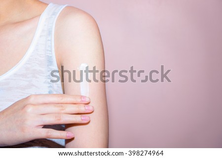 Beautiful young woman with cream on her shoulder. Focus is on a hand with soft pink background