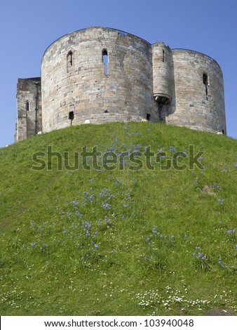 bluebells and daisy flowers growing on the grassy bank beneath a medieval stone round tower of cliffords tower castle in the city of york england
