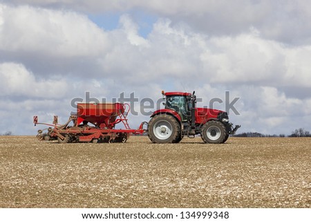 a red tractor and seed drill on a chalky field in the yorkshire wolds england under a cloudy sky in springtime