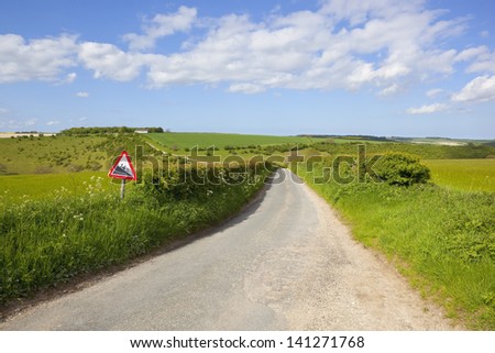 an english country road with sign warning of a steep hill in the yorkshire wolds england amongst arable farmland under a blue cloudy sky in summer