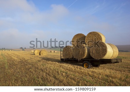 a farm trailer with a stack of round bales in a stubble field in the yorkshire wolds england in late summer under a blue sky