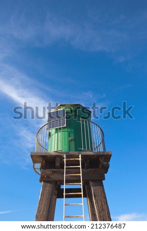 A green wooden navigation light tower fitted with a solar panel to provide power