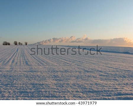 snow covered arable fields under a clear winter sky with the steam from a distant power station on the horizon