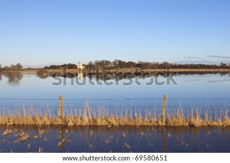 flooded english landscape at derwent ings with a barbed wire fence and distant ancient church surrounded by trees under a blue sky