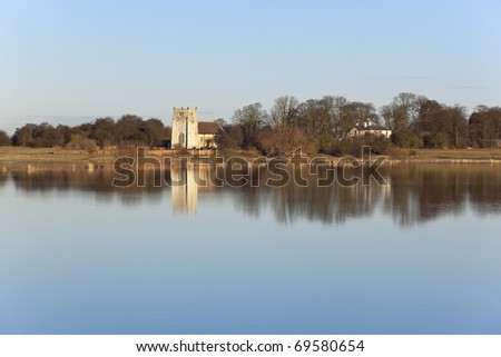 english winter landscape with a view across flooded fields of derwent ings to an ancient church surrounded by trees under a blue sky