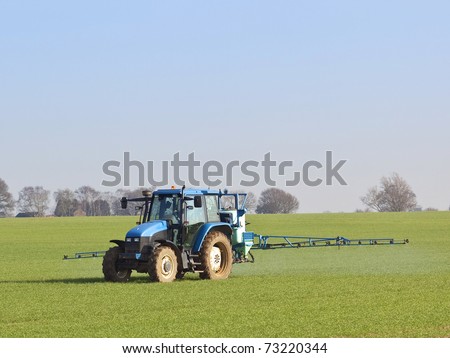 an english landscape with a blue tractor mounted sprayer working on a winter wheat crop on a fine day in february