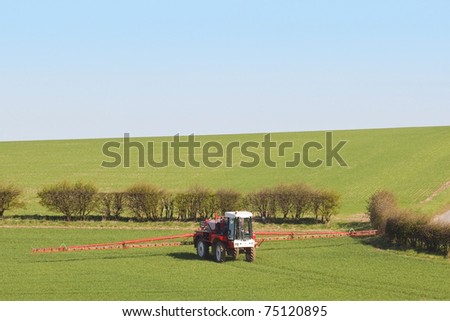 a red crop sprayer in green fields of wheat in springtime under a blue sky