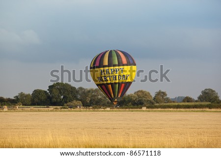 an agricultural landscape with a colorful hot air balloon landing in a stubble field under a cloudy sky in autumn