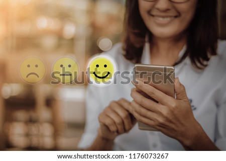 Businesswoman pressing face emoticon on virtual touch screen at smartphone .Customer service evaluation concept.