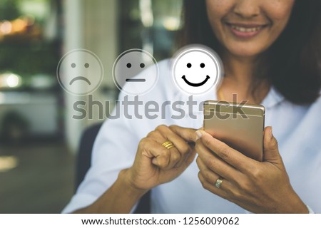 Businesswoman pressing face emoticon on virtual touch screen at smartphone .Customer service evaluation concept.