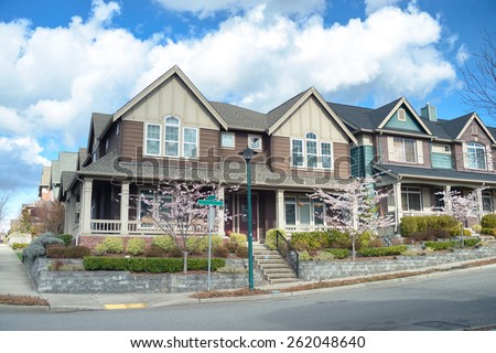 Beautiful two story american houses on the corner of the street. There is porch visible, nice landscaping, sidewalk and spring trees.