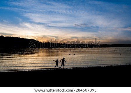 Beautiful sunset. Evening. Two kids holding hands walking in the water. Two birds in the distance.