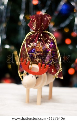 Wooden Christmas elk standing in a cotton snow with red gift sack near decorated tree