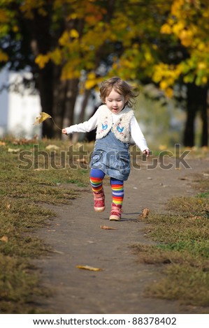 Little girl with autumn leaf running by the path in the park