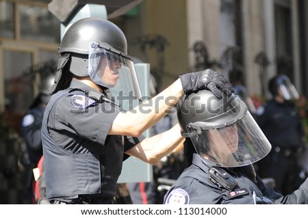 TORONTO-JUNE 25:   A Toronto police officer helps his fellow female colleague to fix her helmet during the G20 Protest on June 25, 2010 in Toronto, Canada.