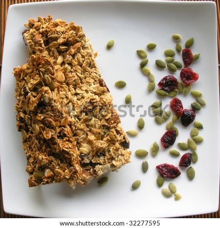 breakfast granola bars on a white squared plate sprinkled with pumpkin seeds and dried cranberries