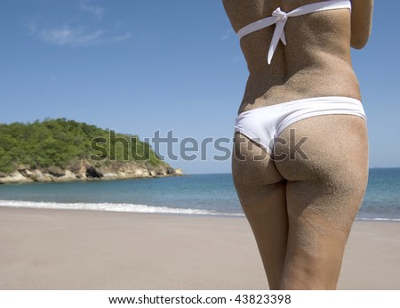 back half length shot of beautiful lady wearing white bikini peacefully looking out over blue water on tropical beach scene in central america