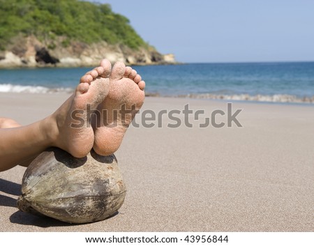 womans feet resting on coconut on tropical beach, guanacaste, costa rica, central america. tranquil carefree vacation holiday getaway on remote exotic seashore island