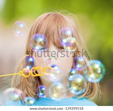 boy with long blond hair blowing soap bubbles