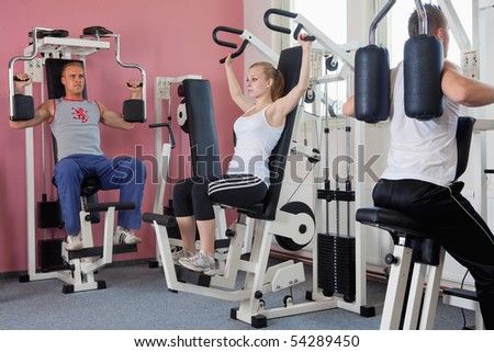 three people exercising on machines at modern gym - health club
