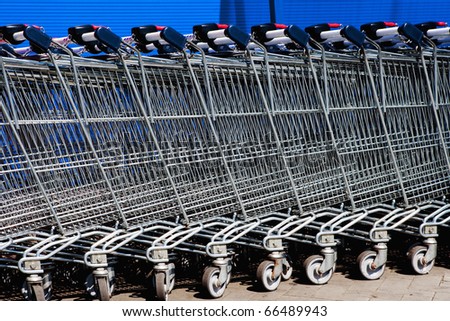 a line of empty supermarket shopping carts against blue wall