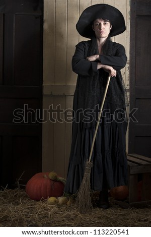old halloween witch with broom and pumpkin in a barn