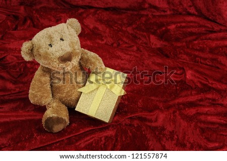 Teddy bear with golden gift box on red background