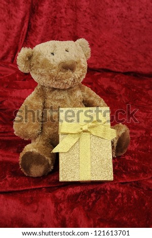 Teddy bear with golden gift box on red background